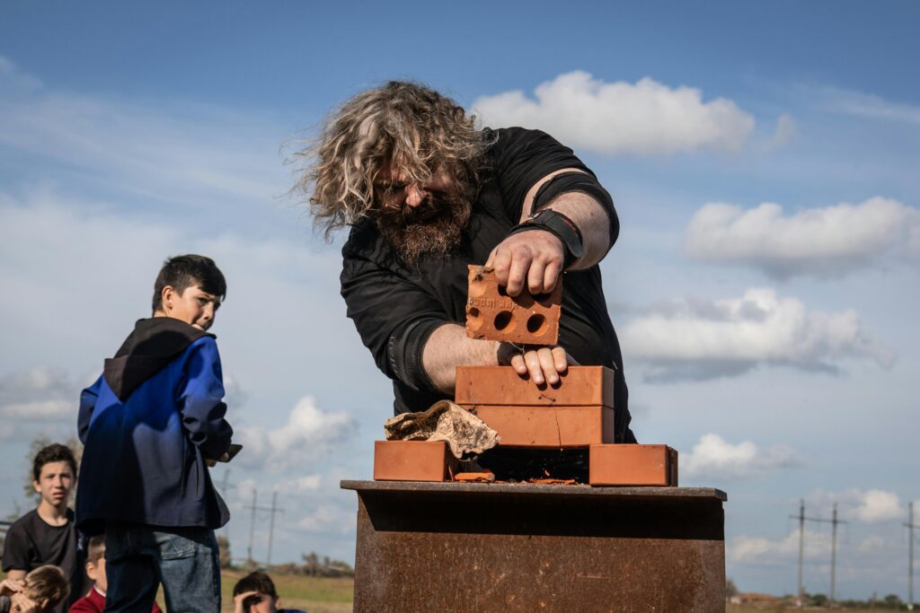 A bearded man shows his strength breaking bricks with spectators around.