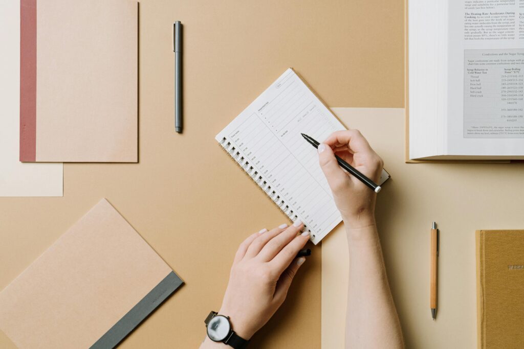 Organized workspace with notebook and hands writing using various stationery.