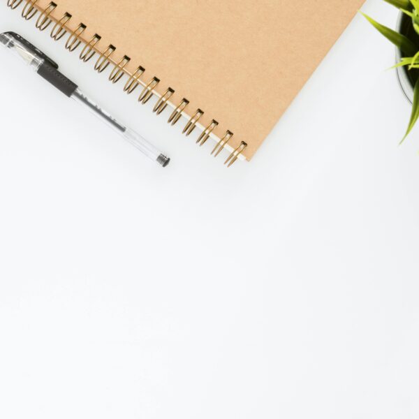 Minimalist stationery setup with a spiral notebook and pen on a clean white desk.