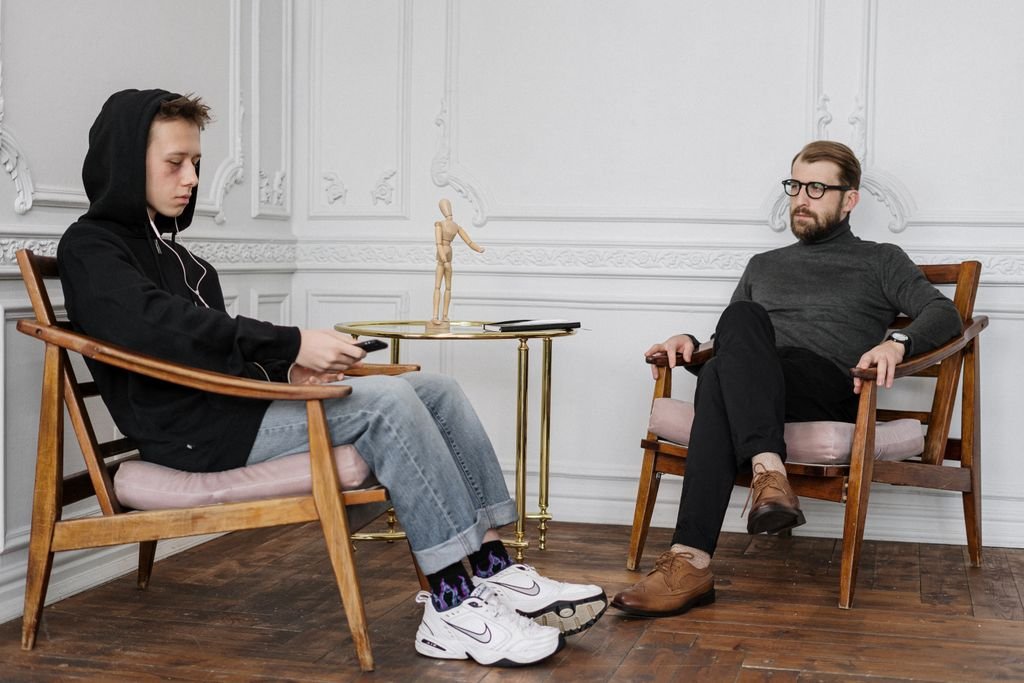 A concerned teenage boy in a hoodie sits with a therapist during a session.