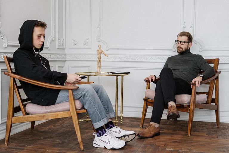 A concerned teenage boy in a hoodie sits with a therapist during a session.