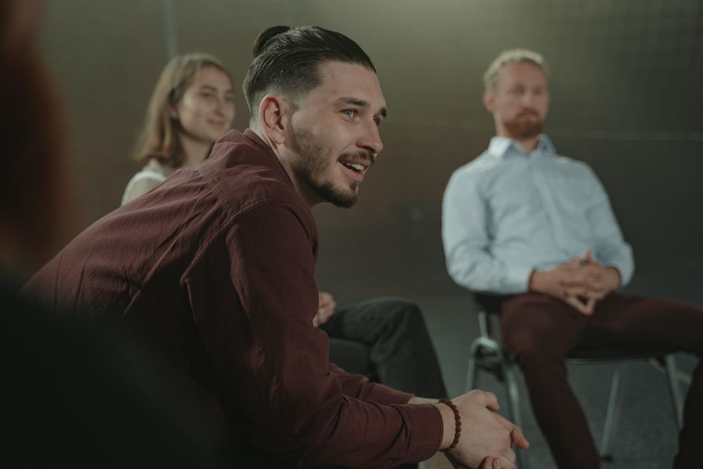 Adults sitting in a circle engaged in a group discussion indoors.
