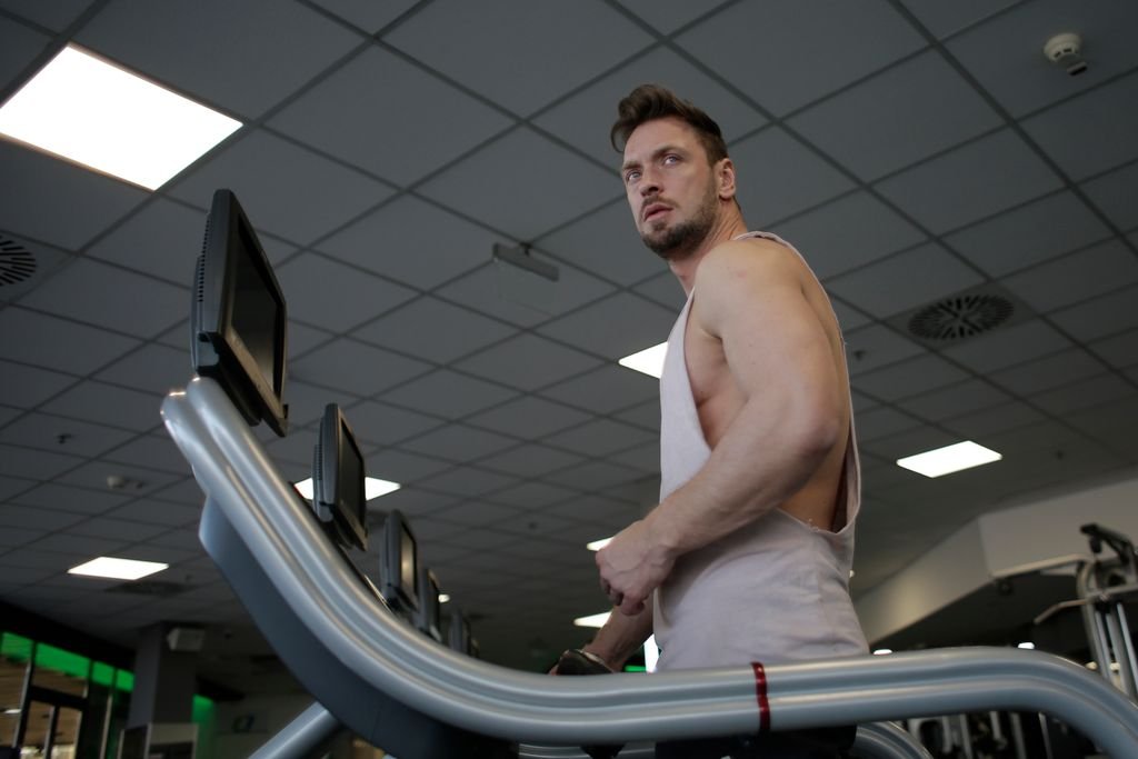 Low angle of muscular adult male athlete in sportswear during training on running machine in modern spacious fitness center while looking away