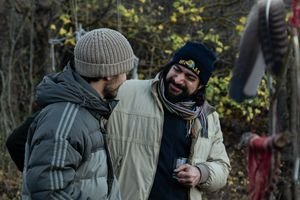 Two men enjoy a friendly chat outdoors, dressed warmly for cold weather.